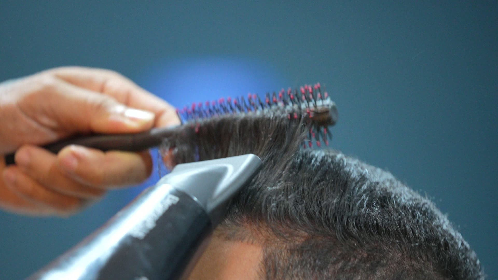 Barbeiro finalizando o penteado de um cliente com escova e secador